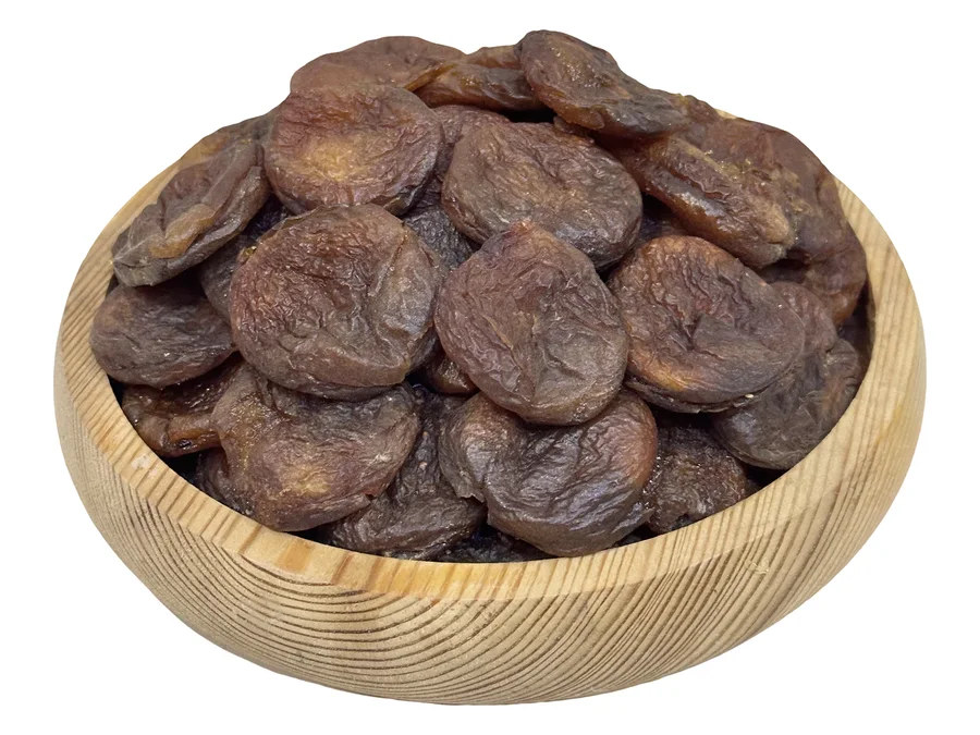 A wooden bowl heaped with unsulphured Armenian dried apricots, deep chocolate-brown, seen at an angle