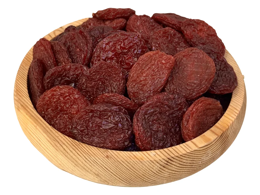 A pine bowl heaped with Armenian dried Rehan plums, deep wine-red to near-black, seen at an angle